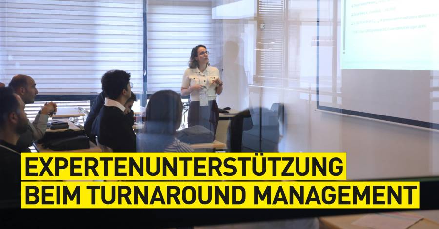 Frau präsentiert vor Publikum in Büroräumlichkeiten. Headline zu Turnaround Management ist zu sehen