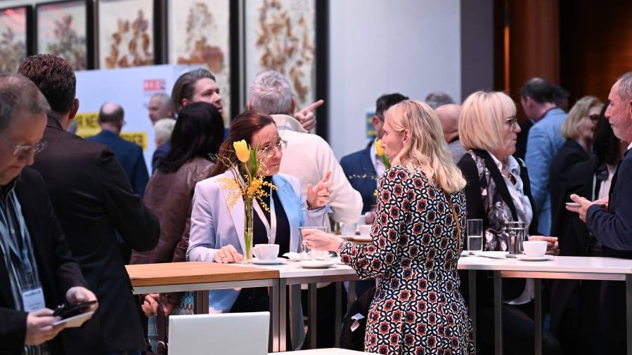 Zwei Frauen im Gespräch an einem Stehtisch mit Kaffee und gelben Blumen
